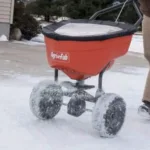 someone dispensing ice-melt salt on a snow-covered yard, using the AGRI-FAB 45-0548 Pro Push Spreader