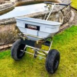 the Cobra HS60S Push Spreader on a lawn, in front of a water feature