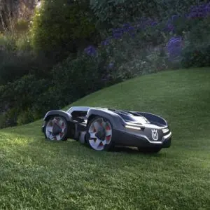 a Husqvarna Automower travelling across an undulating lawn, with plants in the background