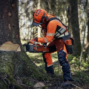 a man dressed in full Husqvarna PPE, using a chainsaw to fell a tree