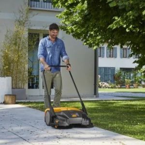 a man clearing leaves from a driveway in a residential area, using the STIGA SWP 577 Push Garden Sweeper