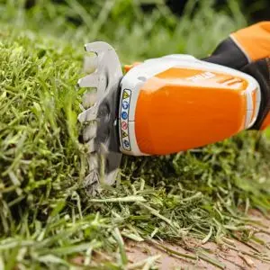the STIHL HSA 26 Shrub Shears, fitted with a lawn edger attachment, cutting grass on the edge of a lawn