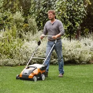 a man wearing safety glasses, pushing the STIHL RLA 240 Cordless Lawn Scarifier across a lawn