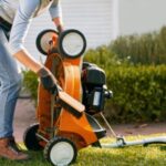 a woman using a brush to clean the underside of an orange STIHL lawnmower