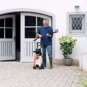 a man stood outside a white house, next to a STIHL pressure cleaner, holding a pressure-cleaning attachment