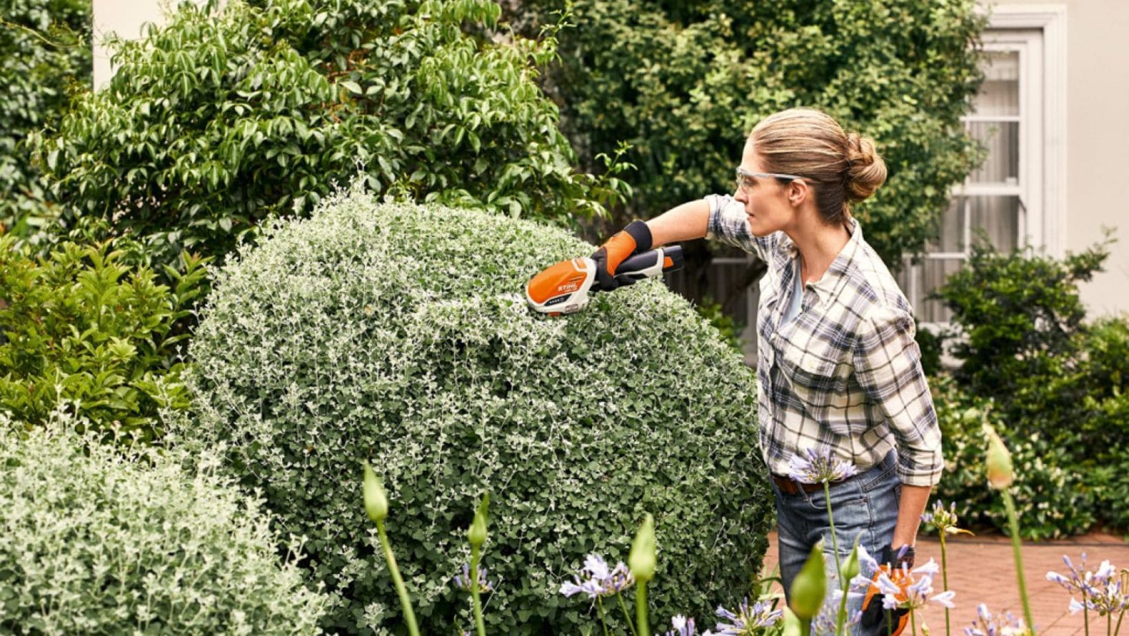 a woman using cordless secateurs to prune an ornamental hedge