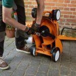 a man using a spanner to remove the blade from underneath an orange STIHL lawnmower