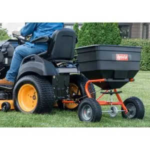 a man sat on a ride-on mower, which is towing a lawn spreader