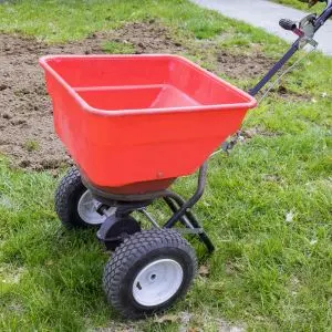 a drop spreader, with a red hopper, positioned on a patchy lawn