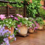 a line of potted plants on brown composite decking, in front of brown slatted panels