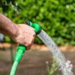 a close up of a man watering a garden using a green hose
