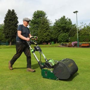 a man wearing a flat cap, pushing the Allett Stirling 51 Cordless Cylinder Mower across a sports pitch