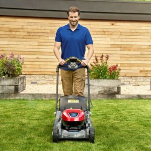 a smiling man, wearing a blur polo shirt, using a Honda HRX to mow a lawn