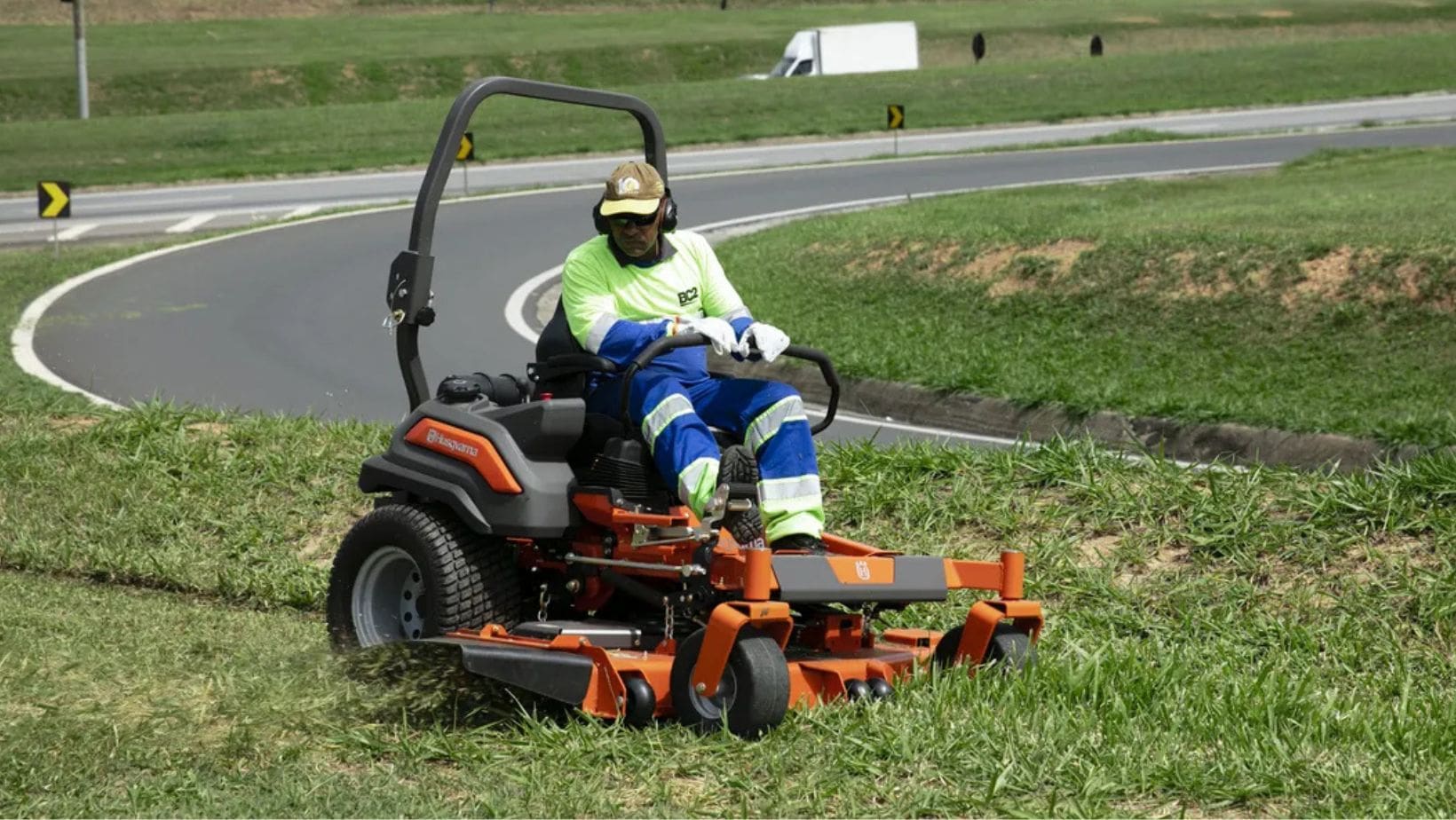 a groundscare worker operating the Husqvarna Z560X Zero-Turn Mower on a grassy verge, on the side of a winding road