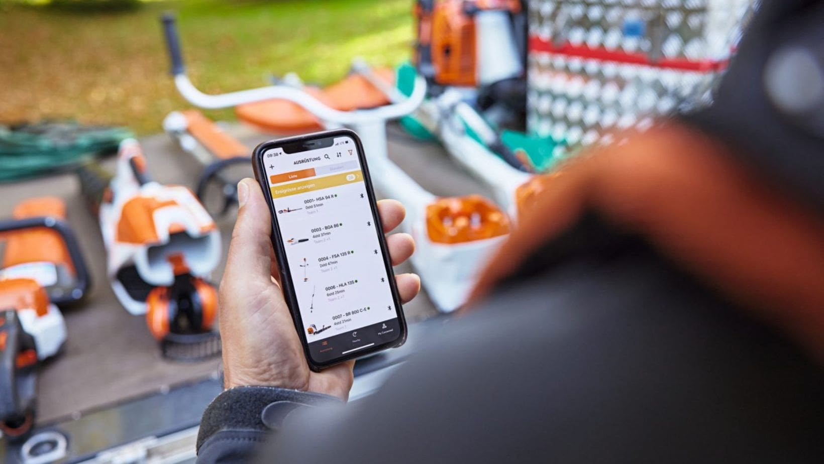 a man stood in front of a range of STIHL tools, using his smartphone to operate the STIHL Connected app