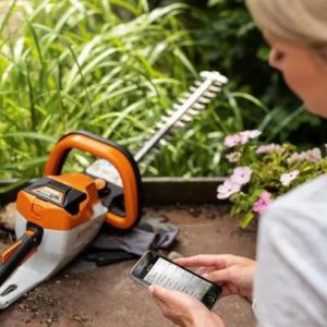 a woman stood next to a STIHL hedge trimmer, using her smartphone to set up the STIHL Connected app