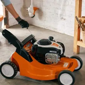 a woman using a thin rod to clean a lawnmower's air filter