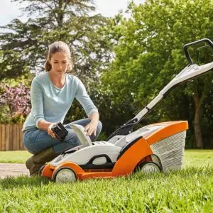 a woman removing the battery from a STIHL cordless lawnmower