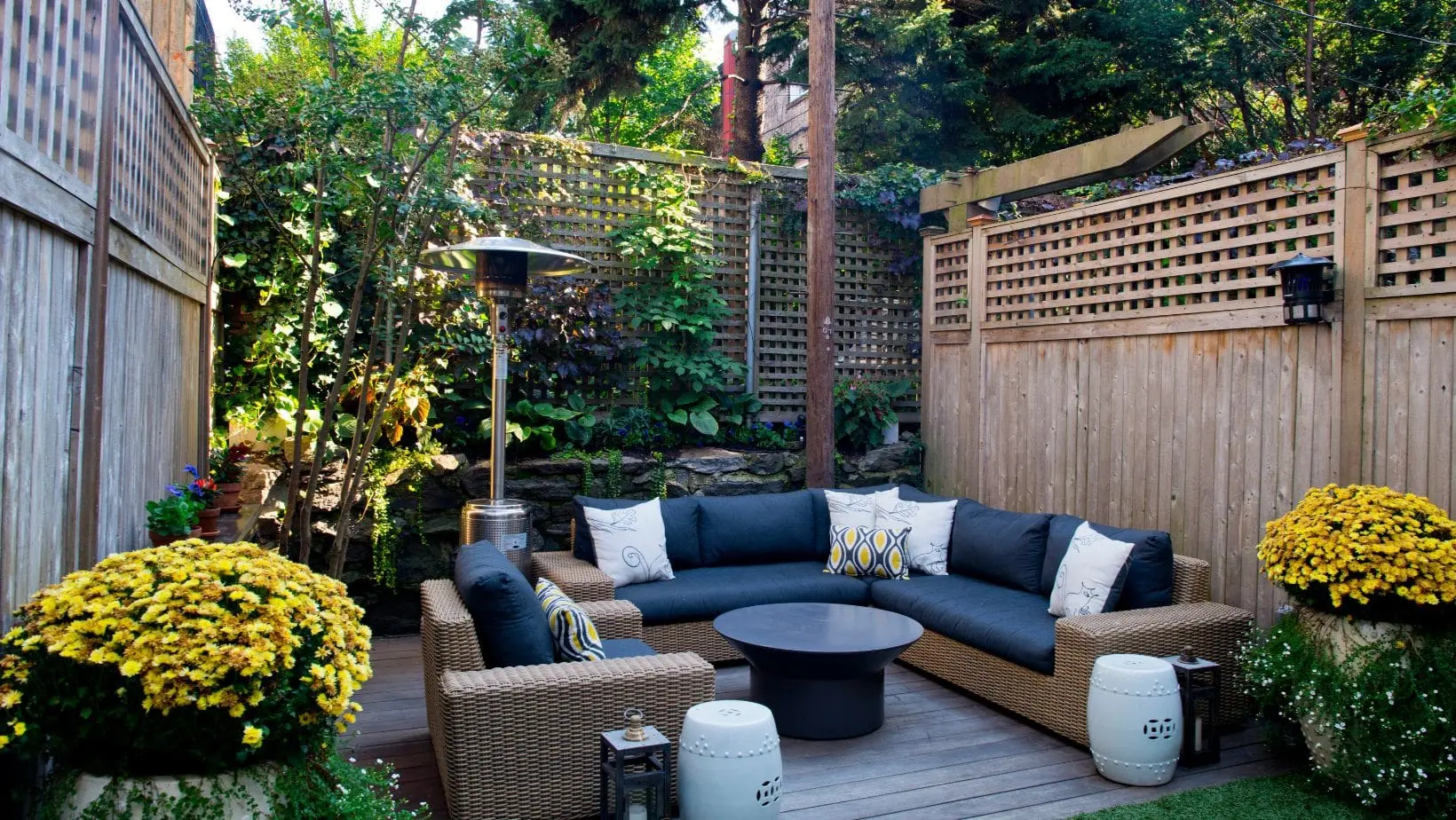 a small garden design including a decked area, outdoor furniture, potted plants, a bird feeder, and trellis