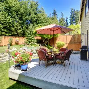 garden seating, a parasol and potted plants on a raised decked area, with a wider garden, fence panels and trees in the background