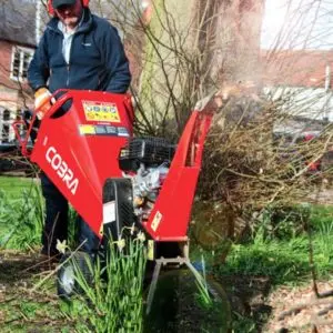 a man shredding green waste in a garden, using the Cobra CHIP650L Petrol Wood Chipper