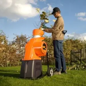 a man wearing a baseball cap, stood near hedging, feeding branches into the Eliet NEO² Electric Garden Shredder