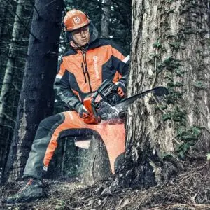 someone wearing full chainsaw PPE, using a Husqvarna chainsaw to fell a tree