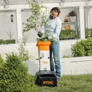 a man feeding tree branches into the STIHL GHE 105 Electric Garden Shredder, with a white orangery in the background