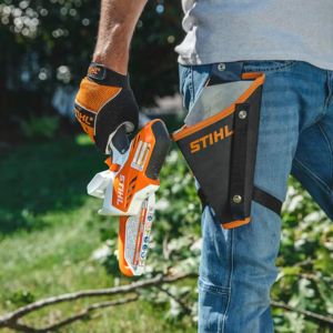 a man holding the STIHL GTA 26 Cordless Pruner next to a STIHL-branded holster, which is attached to his waist