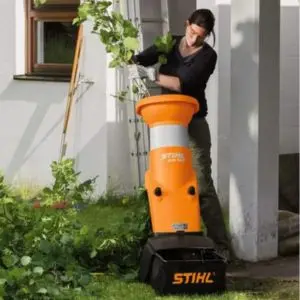 a woman stood near a white house, feeding garden waste into the STIHL GHE 150 Electric Chipper