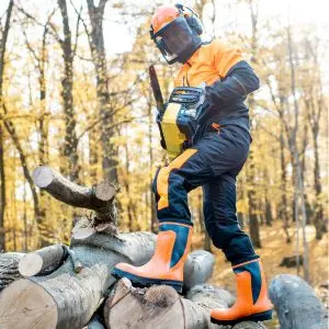a man stood on a pile of logs, dressed in orange and black chainsaw PPE