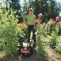 a woman using the Honda Tiller FG110K1 to cultivate soil between rows in a garden bed