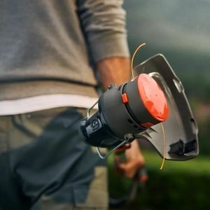 a man stood in a garden, revealing the underside of the Husqvarna Aspire™ T28-P4A Cordless Grass Trimmer