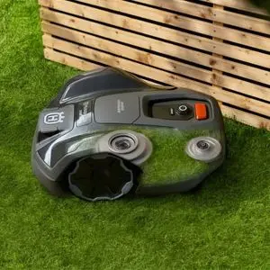 the Husqvarna Automower® 305E NERA mowing a lawn next to a slatted wooden planter