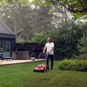 a man using a Husqvarna aerator on a lawn, with a house, patio and trees in the background