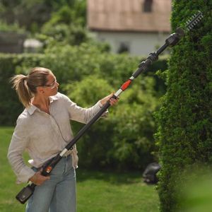 a woman wearing safety glasses, operating a Husqvarna cordless hedge trimmer