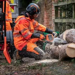 a man crouching down, dressed in orange chainsaw PPE, using the Husqvarna 540i XP Cordless Chainsaw to split a log