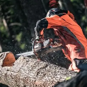 a man dressed in full chainsaw PPE, using the Husqvarna 540i XP Cordless Chainsaw to make precision cuts in a log
