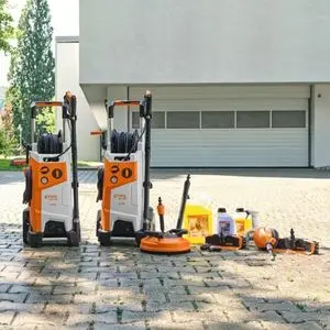 2 STIHL RE 150 PLUS pressure washers, alongside various attachments and detergents, on a paved area outside a white industrial building