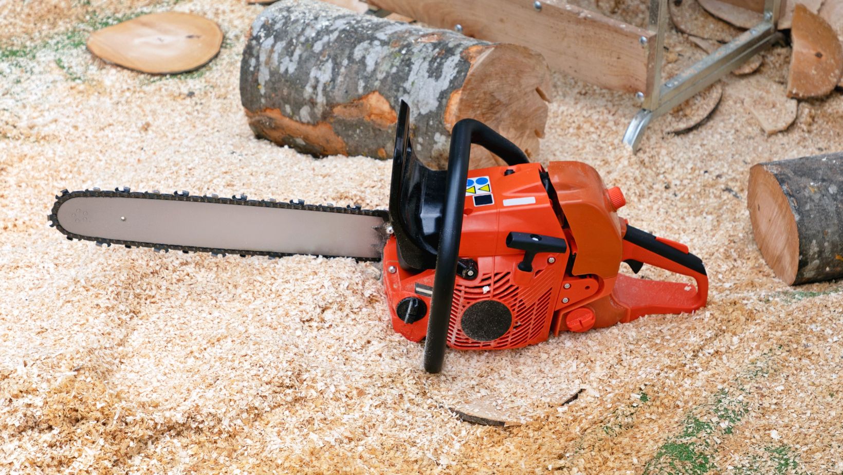 an orange petrol chainsaw sitting in sawdust, next to some logs