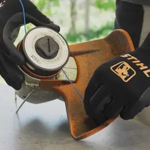 someone wearing STIHL protective gloves, changing the line on a strimmer
