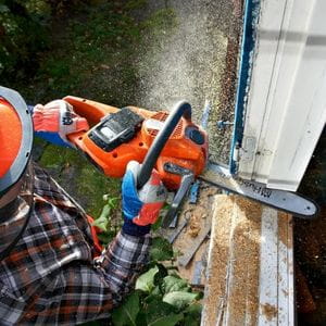 a man wearing helmet, gloves and a checked shirt, using a Husqvarna 535i XP Chainsaw to cut a window frame