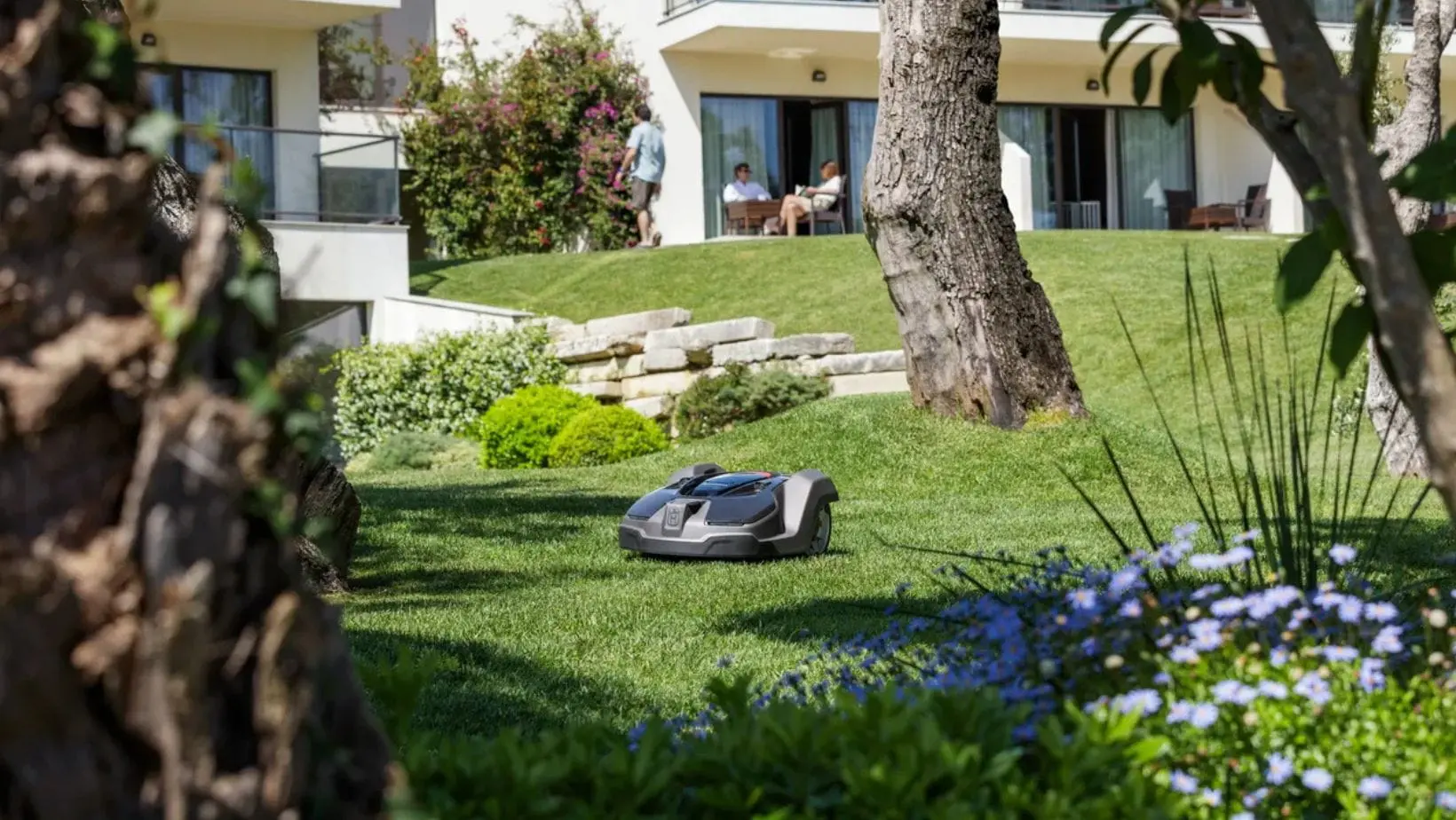 a Husqvarna Automower navigating a complex garden, including a slope, steps, trees, and borders