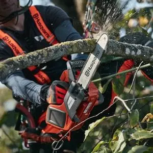 a man in a tree canopy, using a Husqvarna top handle chainsaw to prune a branch