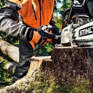 someone in a wood, wearing chainsaw PPE, using a tool to tension a STIHL chainsaw chain