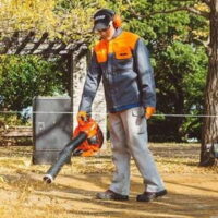 a man wearing ear defenders and a baseball cap, using the ECHO PB2620 Petrol Handheld Leaf Blower in an urban green space