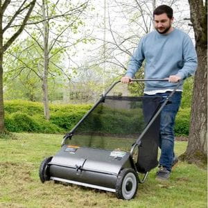 a bearded man pushing the Handy THPLS Leaf Sweeper across a lawn, surrounded by trees and shrubs