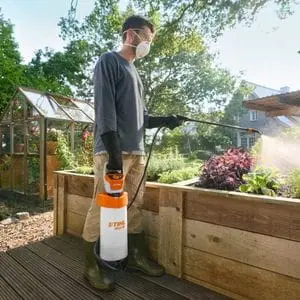 a man wearing a face mask, using the STIHL SGA 30 Cordless Sprayer to apply targeted treatment to plants in a wooden raised bed