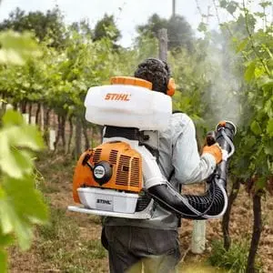 a rearview shot of a man in an orchard, wearing ear defenders, using the STIHL SR 450 Petrol Mistblower to apply treatment to the trees