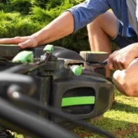 a close up of someone using a screwdriver to access a lawnmower's working parts